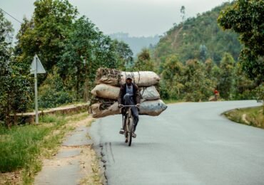 A man skillfully rides a bicycle carrying multiple large bags on an urban street.